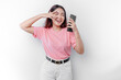 A young Asian woman with a happy successful expression wearing pink t-shirt and holding smartphone isolated by white background