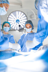 Preparation for the beginning of surgical operation with a cut. Group of surgeons at work in operating theater toned in blue. Medical team performing operation