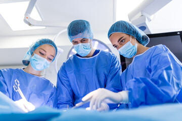 Wall Mural - Group of medical team urgently doing surgical operation and helping patient in theater at hospital. Medical team performing surgical operation in a bright modern operating room