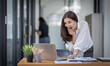 © David - Excited Happy Asian young woman using phone and laptop sitting on a desk office in the day at office