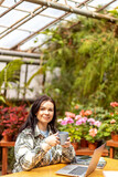 Fototapeta Kwiaty - Woman with a cup of coffee sitting at a table in a greenhouse