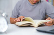 © Pornpimon - Closeup image of Asian woman sitting at a table reading a book in the living room.