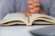 © Pornpimon - Close-up of a woman reading an open bible, praying and holding hands on her bible. Spiritual or bible study concept.