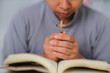 © Pornpimon - Close-up of a woman reading an open bible, praying and holding hands on her bible. Spiritual or bible study concept.