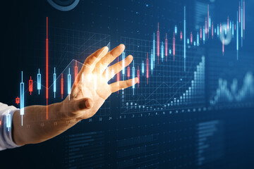 Poster - Close up of male hand using abstract glowing candlestick business chart on blue background. Trade, finance and market concept.