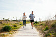© Westend61 - Happy mature couple running on pathway at beach