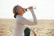© Westend61 - Woman sitting and drinking from water bottle at beach