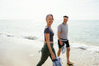 © Westend61 - Smiling woman walking with man holding sports shoes at beach