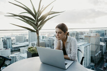 Woman With Hand On Chin Sitting With Laptop On Rooftop