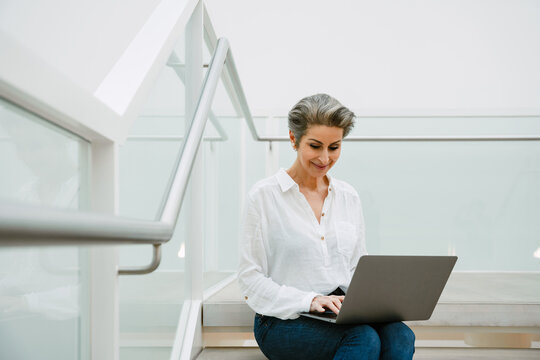 Smiling mature woman manager working on laptop while sitting in art gallery