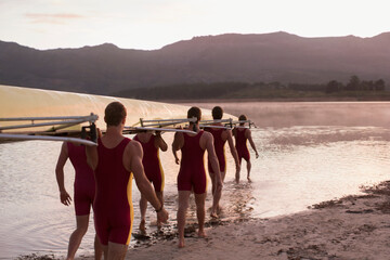 Rowing team carrying scull into lake at dawn