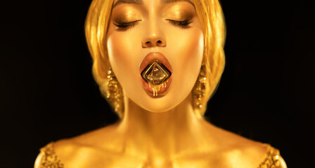 Portrait closeup Beauty fantasy woman sexy mouth hold diamond liquid gold drops drip on lips face in golden paint shiny skin. Fashion model sexy girl metallic makeup. creative jewellery. black studio