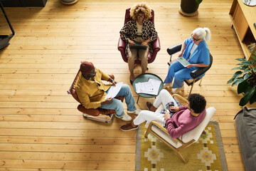 Leinwandbilder - Above view of four intercultural brokers in smart casualwear having discussion of papers or working points at meeting in office