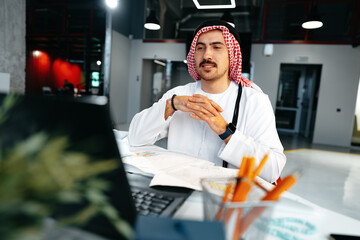 Poster - Young muslim businessman in traditional outfit working at the table in office