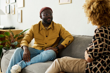Poster - Young confident African American male manager looking at female colleague while sitting on couch in office during conversation