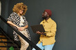 © pressmaster - Two young African American colleagues in casualwear standing on staircase and discussing online data while one of them using laptop