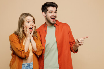 Young shocked surprised couple two friends family man woman wears casual clothes look aside point index finger on area together isolated on pastel plain light beige color background studio portrait.