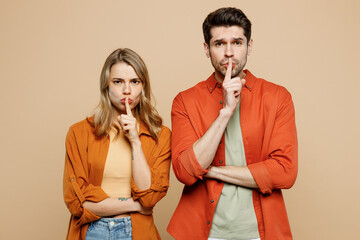 Young secret couple two friends family man woman wear casual clothes say hush be quiet with finger on lips shhh gesture together isolated on pastel plain light beige color background studio portrait.