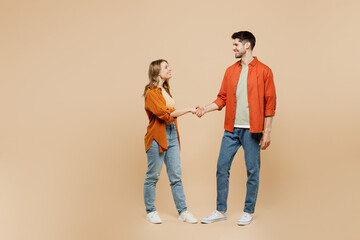 Wall Mural - Full body side view young smiling fun couple two friends family man woman wear casual clothes looking to each other shaking hands together isolated on pastel plain light beige color background studio.