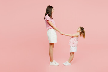 Wall Mural - Full body side view fun happy smiling cool woman wear casual clothes with child kid girl 6-7 years old. Mother daughter hold hands isolated on plain pastel pink background. Family parent day concept.