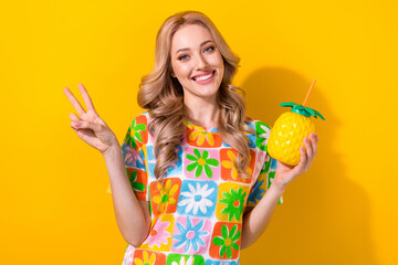 Sticker - Portrait of cheerful pretty cute woman wear flower print t-shirt hold pineapple mug showing v-sign isolated on yellow color background