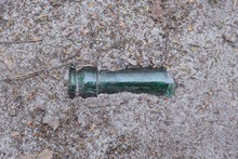 A Piece Of The Neck Of A Green Glass Bottle Lies On The Gray Ground On The Street