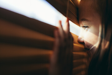 Young girl looking through blinds