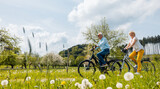 Fototapeta  - Senior coSenior couple riding bicycles in spring through a meadowuple riding bicycles in spring