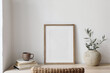 Closeup of picture frame, poster mockup. Vase with olive tree branches on wooden table. Blurred rattan chair. Cup of coffee, books. Summer artistic Mediterranean interior. Working space, home office.