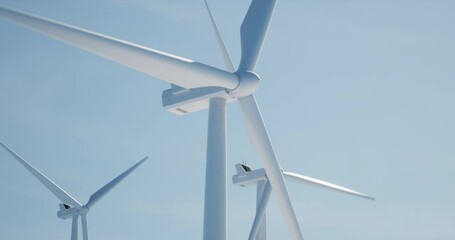 seamless loop clean shot of 3 of wind turbines producing electricity against bright blue sky. backgr