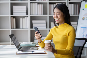 Wall Mural - A young woman is a start-up businesswoman, she sits in the office and uses mobile phones, manages and runs her business from a young generation. Startup business management concept.