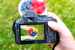 Trzymany w dłoni aparat fotograficzny, na ekranie z podgladem ma żywo miska pełna owoców 