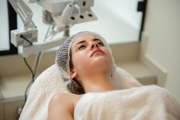 Wall Mural - Headshot of beautiful woman wearing protective cap lying on massage table at luxury spa