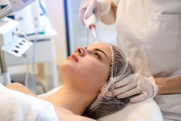 Wall Mural - Close up of young woman receiving electric darsonval facial massage after procedure at beauty clinic.