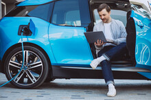 Man Sitting In Electric Car And Working On Laptop