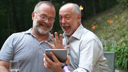 Two gay men have video chat on tablet computer with friends showing their engagement ring for their marriage.