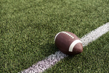 American Football Ball On Green Grass Field Background.