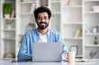 © Prostock-studio - Handsome Young Indian Man Sitting At Desk With Laptop At Home