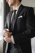 © LIGHTFIELD STUDIOS - cropped view of groom in formal wear with classy black tie and white shirt standing in modern hotel room while adjusting handcuffs, groom on wedding day, special occasion