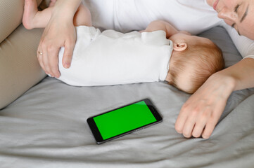 Cute baby and mother hugging sleep at home in bed next to phone, color key. Child safety and protection, co-sleeping