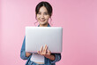 Young Asian college student working with a laptop computer, looking directly at the camera in a studio shot on a pink background