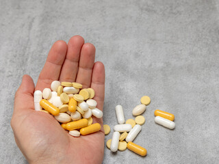 woman hand with many pills tablets in palm,different color and shape,capsules.one pill on girl female finger.medicine treatment concept, antibiotics,vitamins.gray tiles back.stack plastic blisters