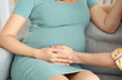 © Pixel-Shot - Young pregnant couple sitting on sofa at home, closeup