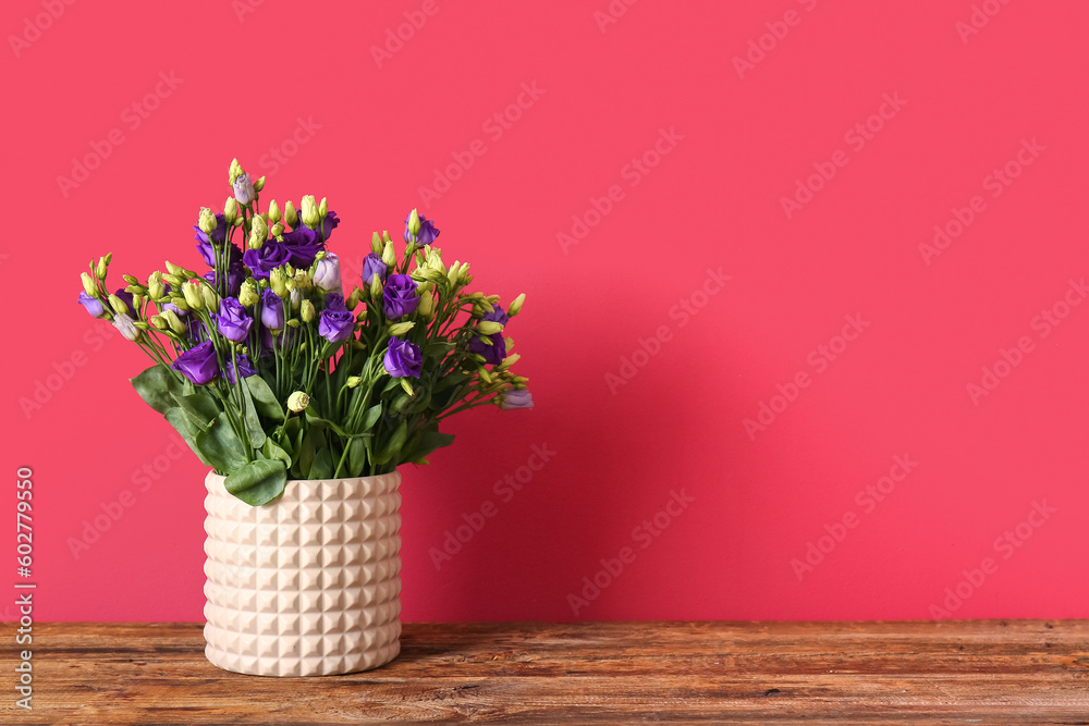 Vase with eustoma flowers on wooden table near red wall