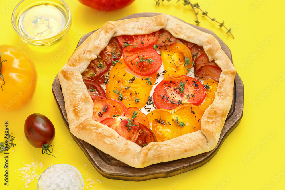 Board with tasty tomato galette on yellow background