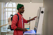 © DimaBerlin - Student African man using self-service electronic terminal to pay for goods in store without salesperson. Self-sufficient black guy standing indoors at college using touch screen vending machine