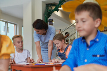 Creative kids during an art class in a daycare center or elementary school classroom drawing with female teacher.