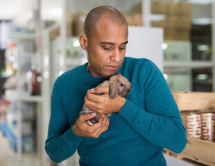 Young adult man choosing new pet in store, holding cute rabbit