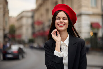Fashion woman portrait smile with teeth standing on the street in front of the city tourist in stylish clothes with red lips and red beret, travel, cinematic color, retro vintage style, urban fashion.