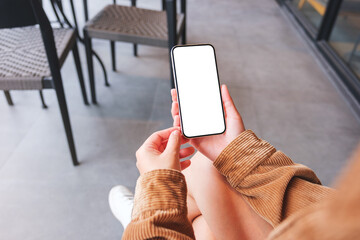 Mockup image of a woman holding mobile phone with blank desktop screen in cafe